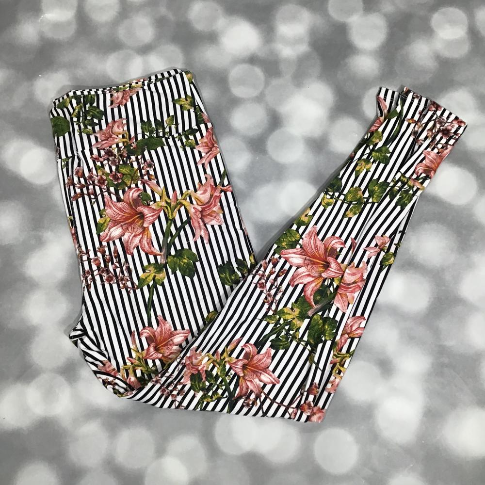 Leggings with black and white striped pattern and pink floral design on a blurred gray background