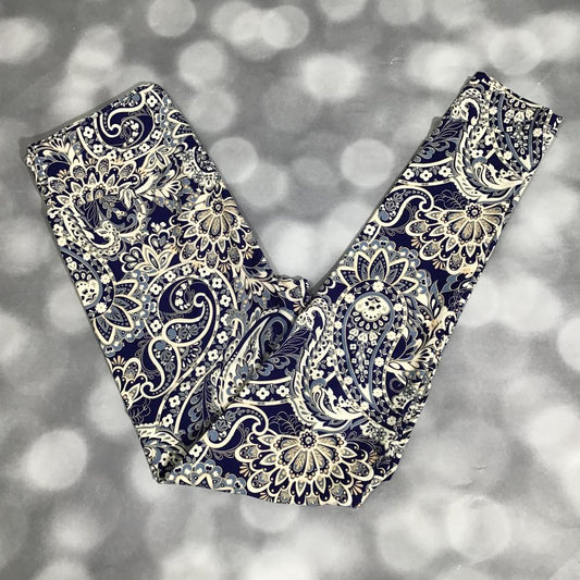 Flat lay of LuLaRoe leggings in navy background with intricate cream and blue paisley floral print, yoga waistband, and ankle-length cut