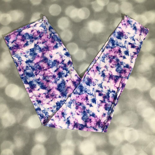Flat lay of LuLaRoe leggings with purple and blue watercolor tie-dye pattern on white base, yoga waistband, and ankle-length silhouette on a blurred background