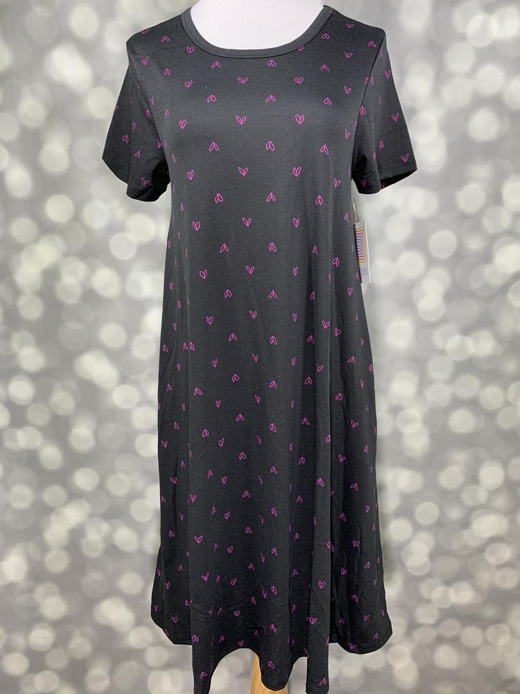 Front view of LuLaRoe Jessie dress on mannequin in black with allover pink mini heart pattern, short sleeves, and flowy swing fit against a blurred background