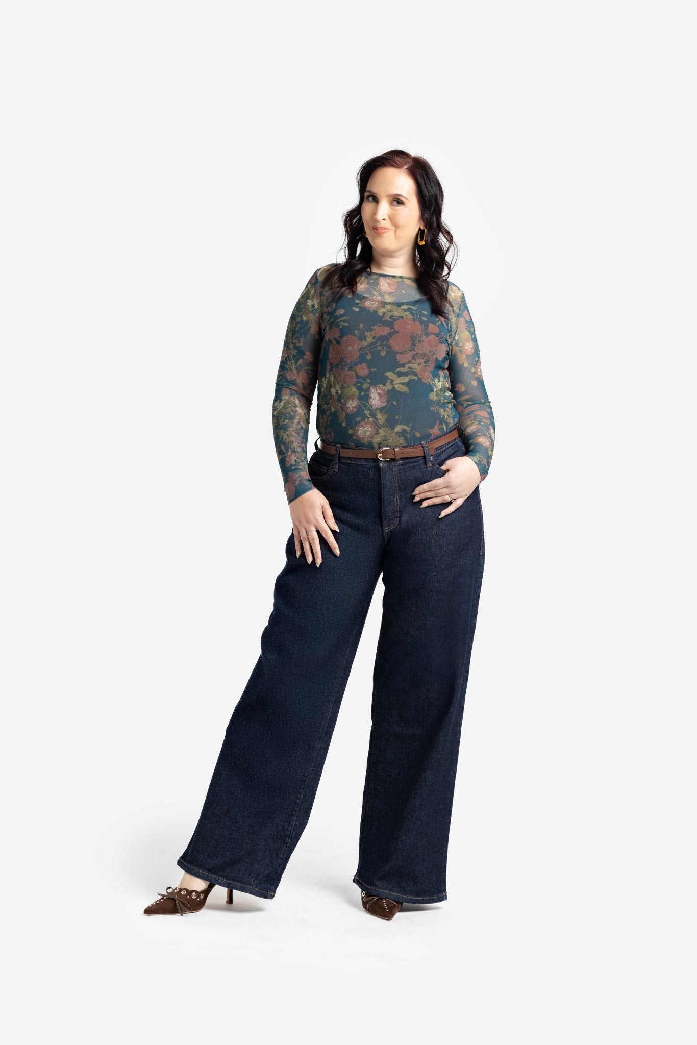 Woman wearing a patterned top and dark jeans on a white background