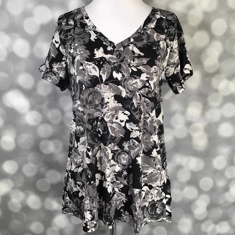 LuLaRoe Christy Tee featuring an allover black, charcoal gray, silver gray, and ivory floral botanical print with layered roses, leaves, and blossoms on a black background. Women's relaxed fit V-neck short sleeve boutique top with elegant monochrome floral design.