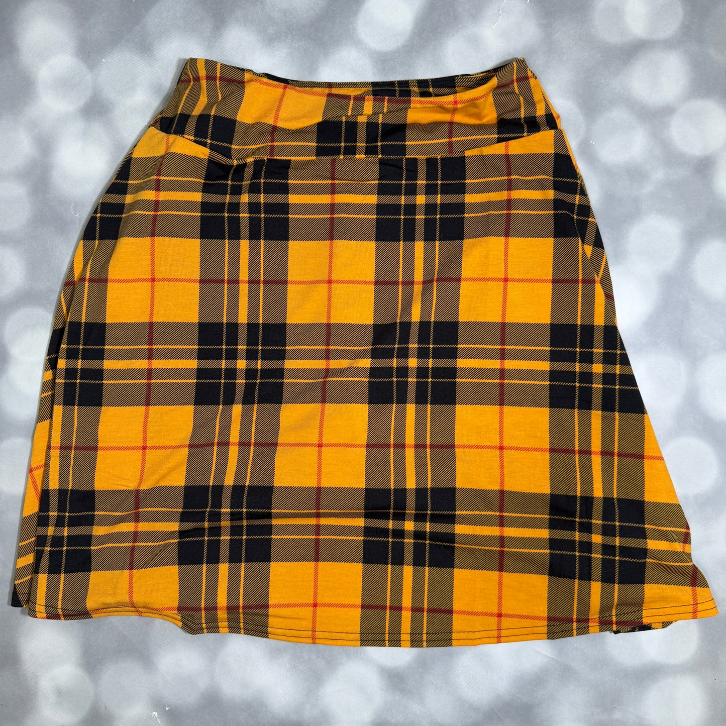A yellow and black plaid skirt laid flat against a gray bokeh background.