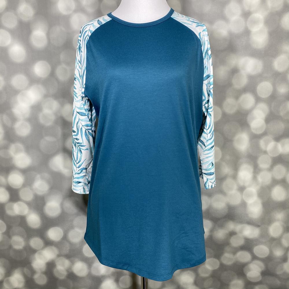 LuLaRoe Randy Tee in Coastal Sage Breeze featuring a deep teal body with ivory raglan sleeves printed with watercolor botanical leaves in teal and sage green in size Large.