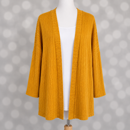 LuLaRoe Connie Lightweight Overlay in Solid Mustard featuring a lightweight cable knit texture, open front cardigan, relaxed fit, and long sleeves layered over a white ribbed tank.