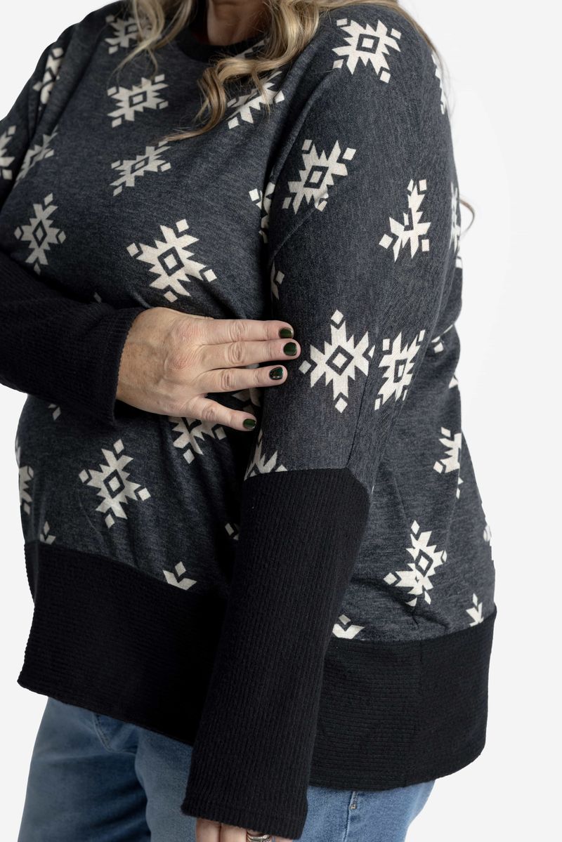 Person wearing a dark sweater with white snowflake patterns on a plain background