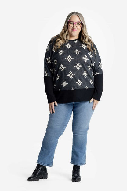 Woman wearing a black and cream aztec patterned sweater and blue jeans on a white background