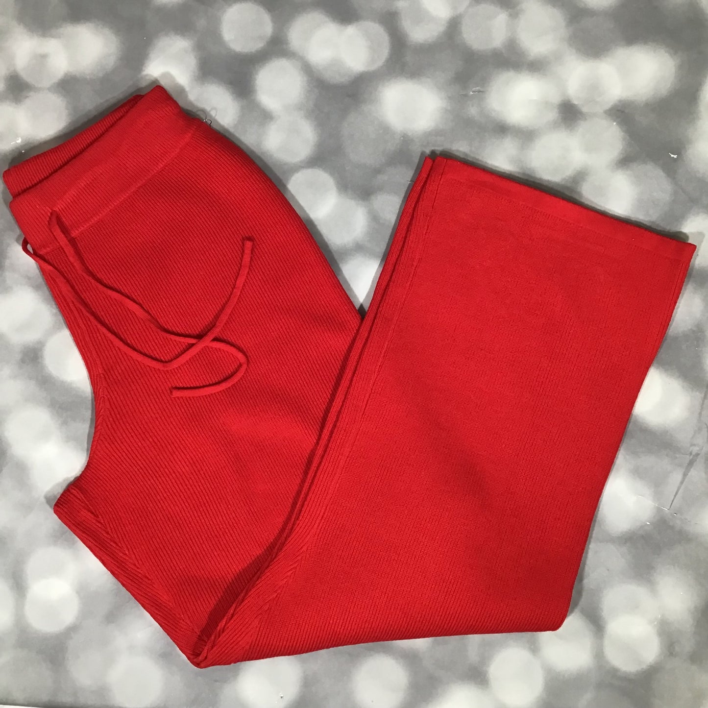 Flat lay of the LuLaRoe Carma Bottom in solid bright red, featuring a wide ribbed waistband, adjustable drawstring tie, soft micro rib knit texture, and relaxed full-length legs on a gray background with a bokeh effect