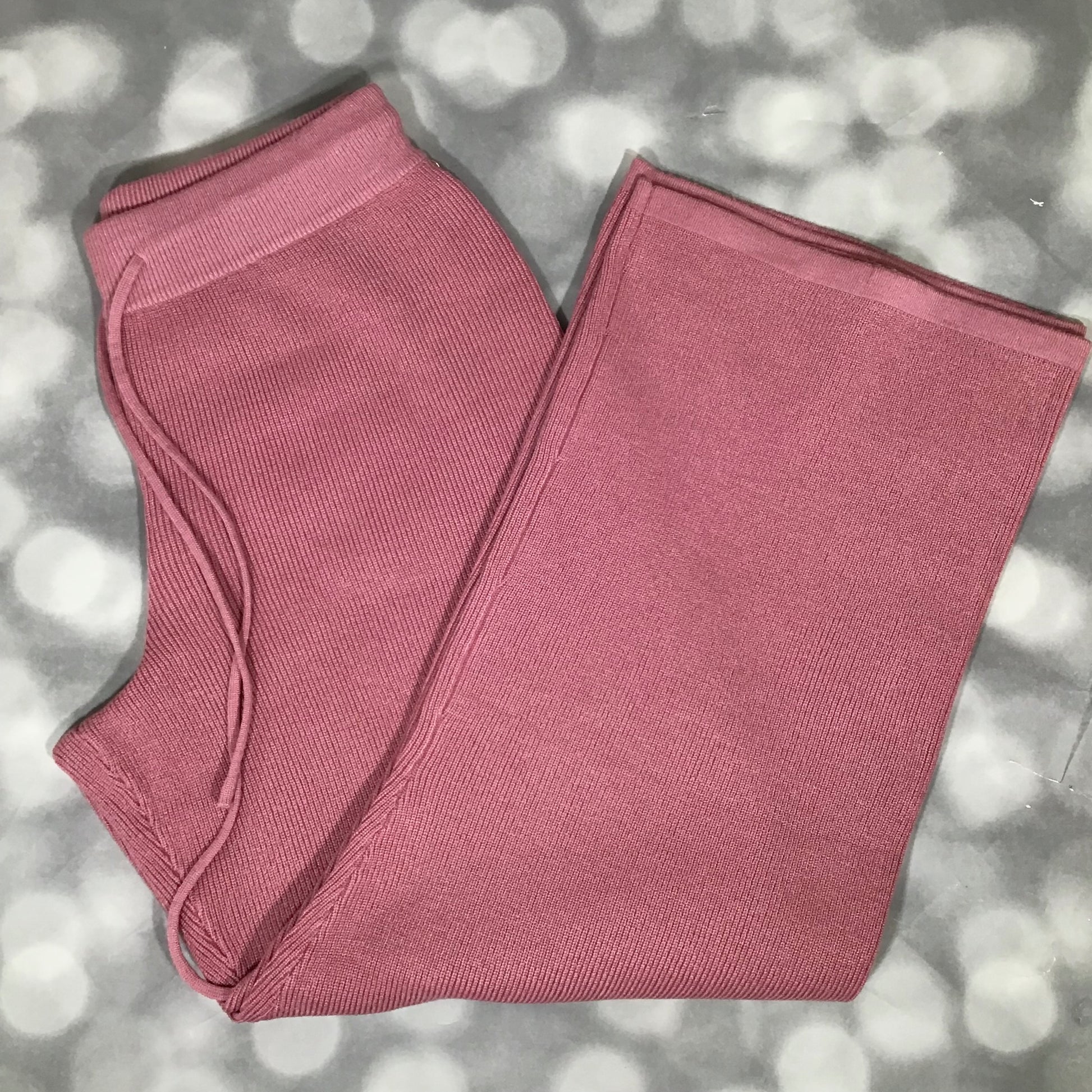 Flat lay of the Carma Bottom in a solid rosy blush pink color, showing the ribbed waistband with drawstring, relaxed full-length leg, and soft micro rib sweater knit texture on a gray bokeh background