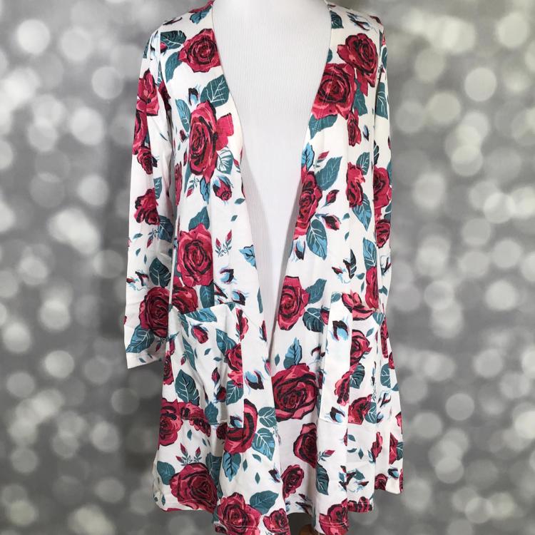 Front view of LuLaRoe Caroline cardigan displayed on mannequin featuring white background with red rose and green leaf floral pattern, open front, and two patch pockets