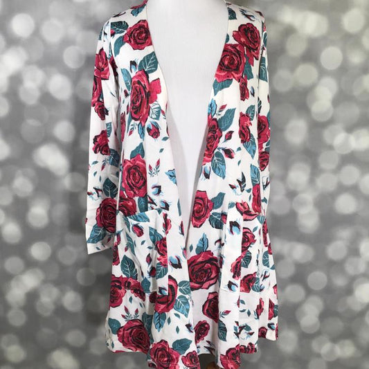 Front view of LuLaRoe Caroline cardigan displayed on mannequin featuring white background with red rose and green leaf floral pattern, open front, and two patch pockets