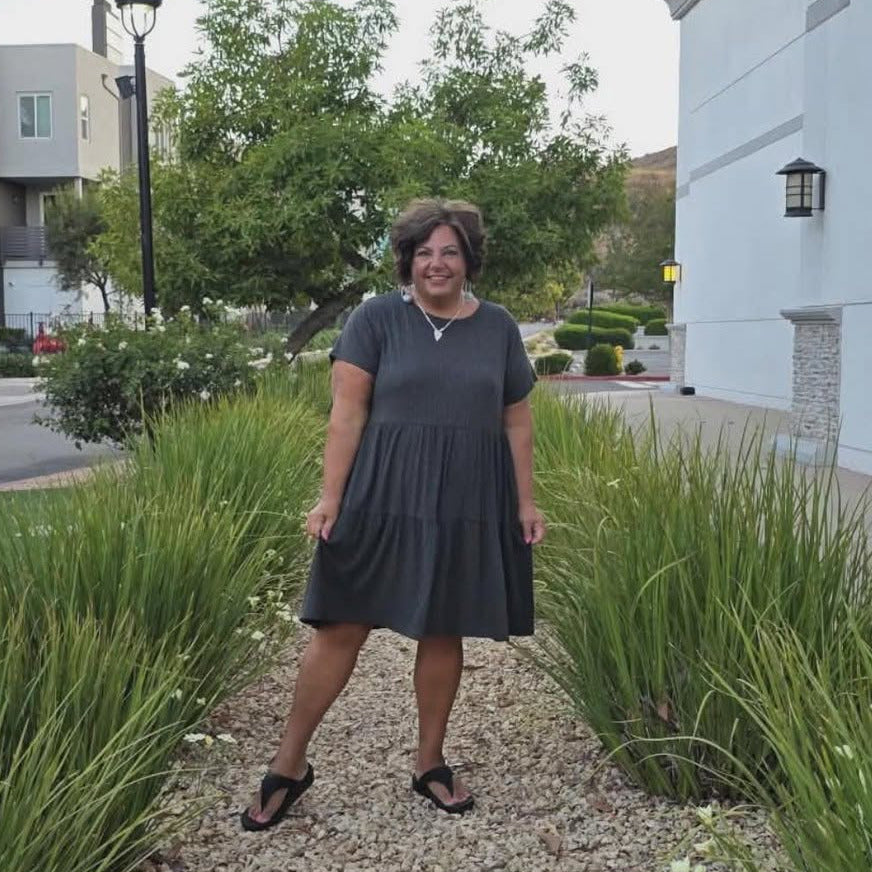 Woman standing on a gravel path between grassy areas with buildings in the background