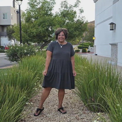 Woman standing on a gravel path between grassy areas with buildings in the background