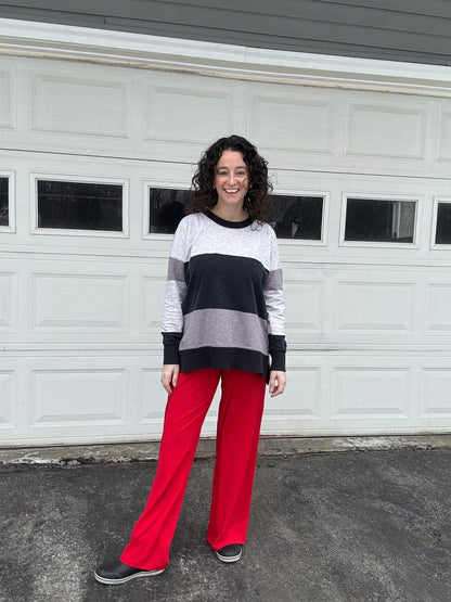 LuLaRoe Essential Wide Leg Pant in solid true red featuring relaxed wide-leg silhouette and comfortable pull-on waistband on a person wearing a striped sweater standing in front of a white garage door.