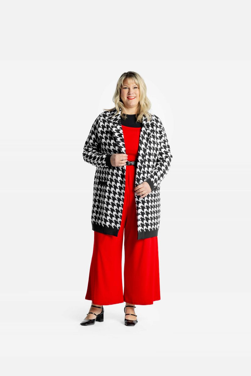 Model wearing a black and white Classic Houndstooth Laura lapel open cardigan with front pockets with red pants on a white background