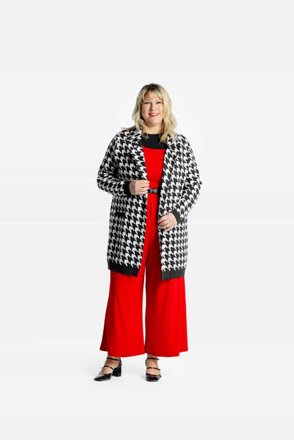 Model wearing a black and white Classic Houndstooth Laura lapel open cardigan with front pockets with red pants on a white background