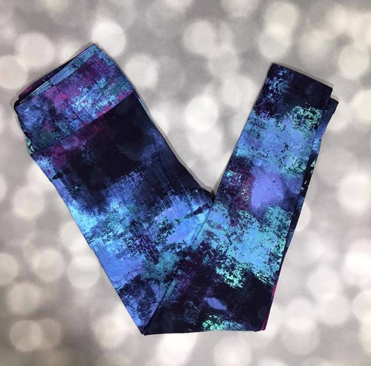 Flat lay of LuLaRoe leggings in black, blue, and multi-color textured abstract pattern with yoga waistband and ankle-length silhouette