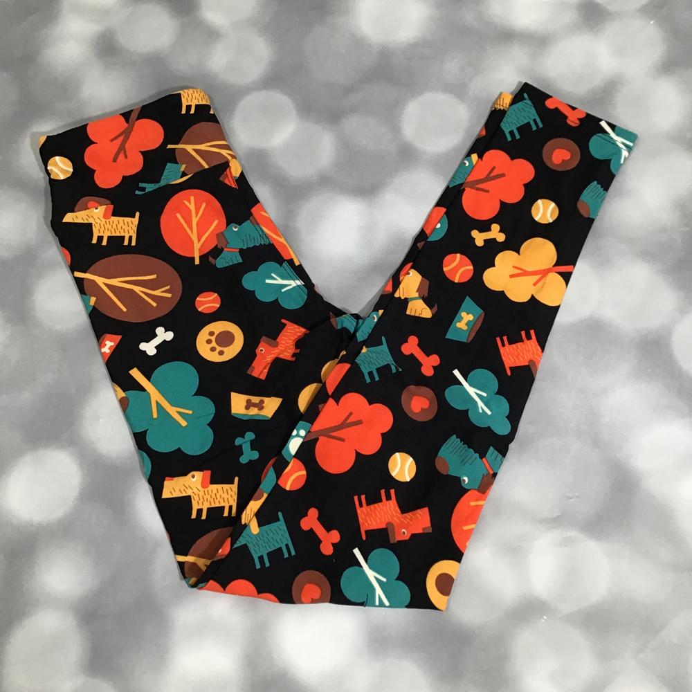 Flat lay of LuLaRoe leggings in black with playful dog park print featuring colorful dogs, trees, bones, and paw prints