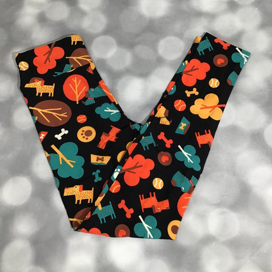 Flat lay of LuLaRoe leggings in black with playful dog park print featuring colorful dogs, trees, bones, and paw prints