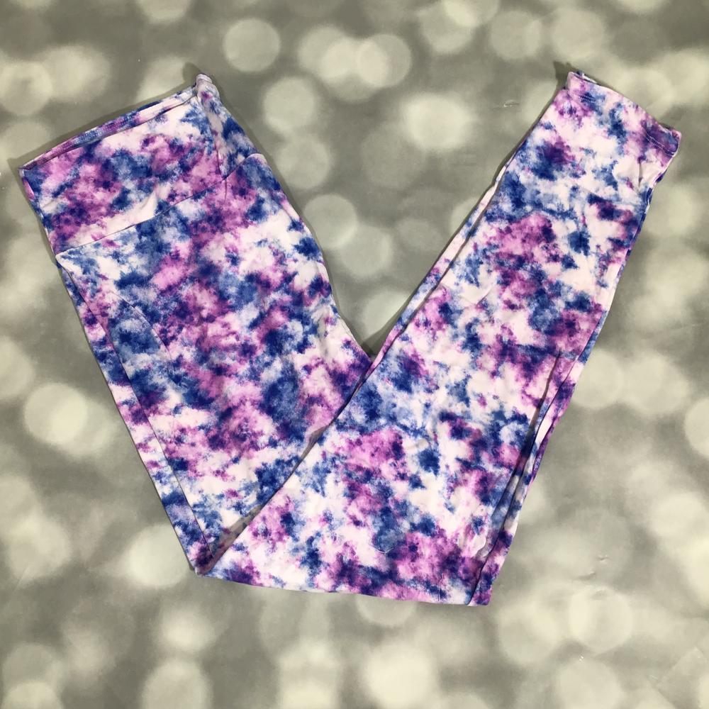 Flat lay of LuLaRoe leggings with purple and blue watercolor tie-dye pattern on white base, yoga waistband, and ankle-length silhouette on a blurred background