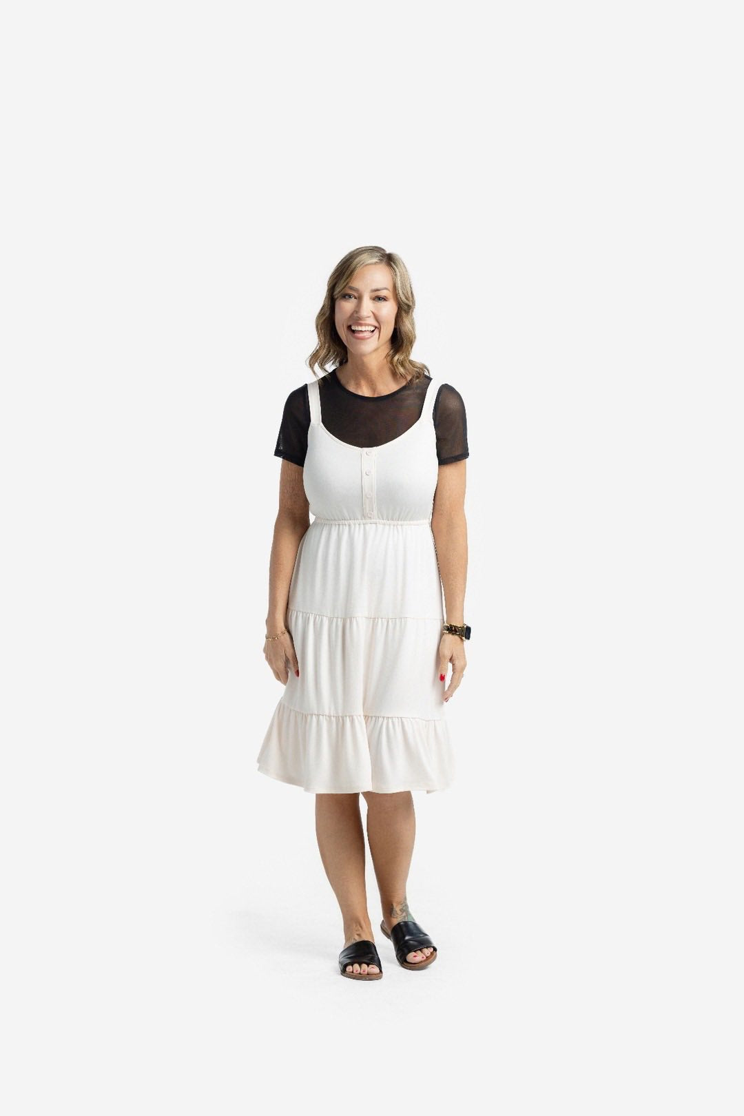 Woman modeling the LuLaRoe Amanda Dress in Solid Soft Ivory, featuring a creamy ivory sleeveless tiered midi silhouette layered over a black mesh short sleeve top against a light neutral studio background.