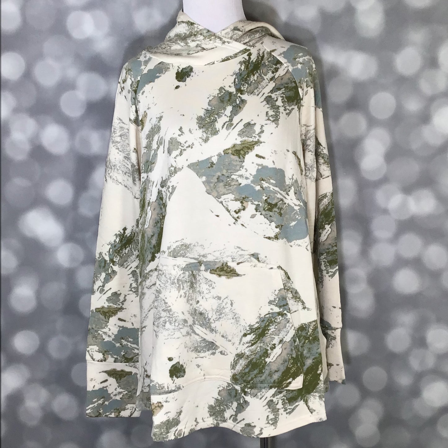 LuLaRoe Amber Hoodie in Sage Stonewash Abstract with ivory base and soft sage green and gray abstract brush pattern, hooded neckline, and kangaroo pocket featuring relaxed fit, long sleeves, soft stretch fabric on a mannequin against a blurred gray background