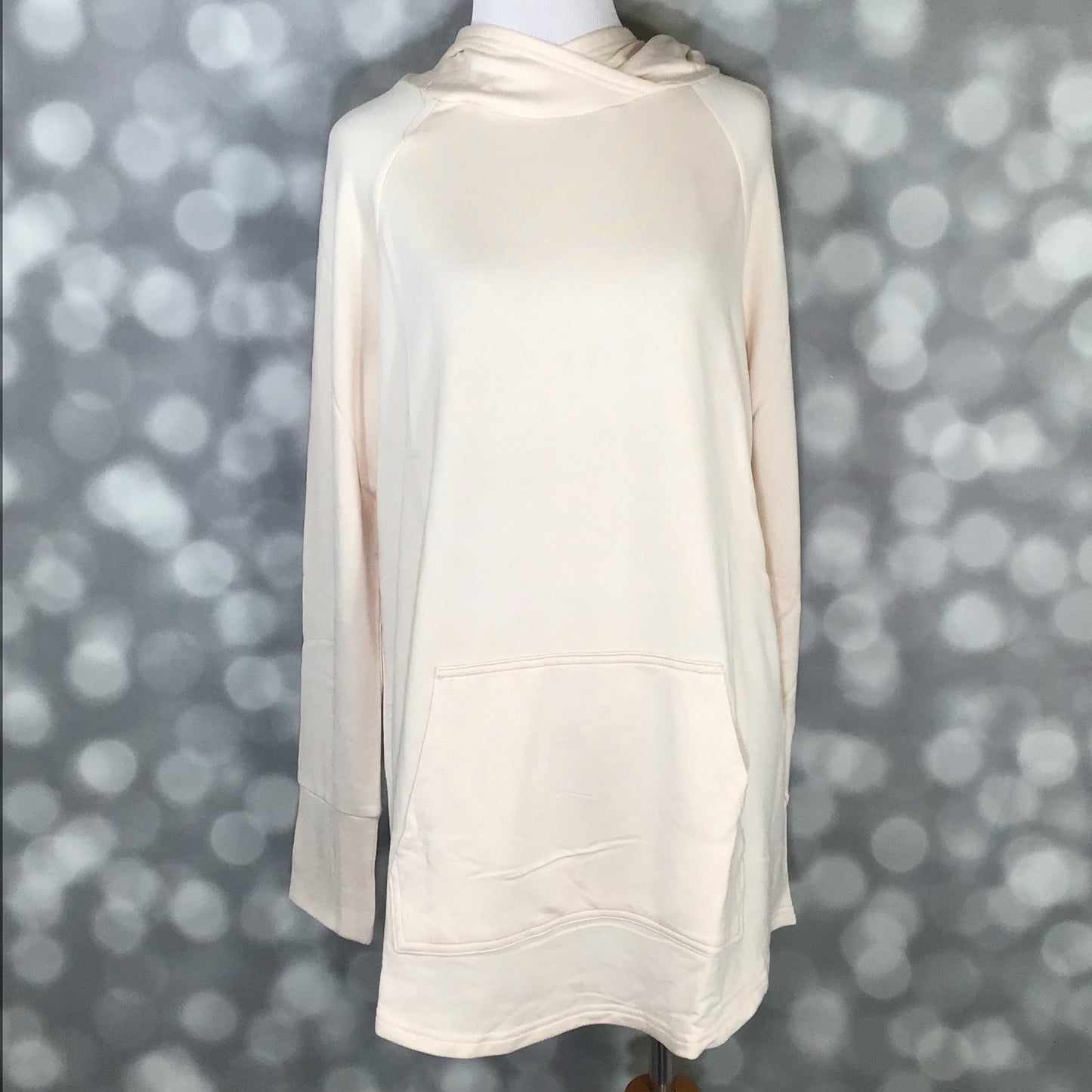 LuLaRoe Amber Hoodie in Solid Soft Porcelain Cream with relaxed fit, hooded neckline, and kangaroo pocket, front view featuring soft stretch fabric, long sleeves, and longer-length silhouette on a mannequin against a blurred gray background