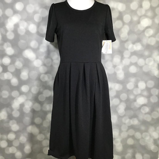 LuLaRoe Amelia Dress in solid black featuring a fitted bodice, short sleeves, flattering waist seam, box pleated full skirt, and hidden side pockets. Women's classic black fit and flare dress designed for workwear, special occasions, business casual outfits, travel wardrobes, and timeless year-round styling