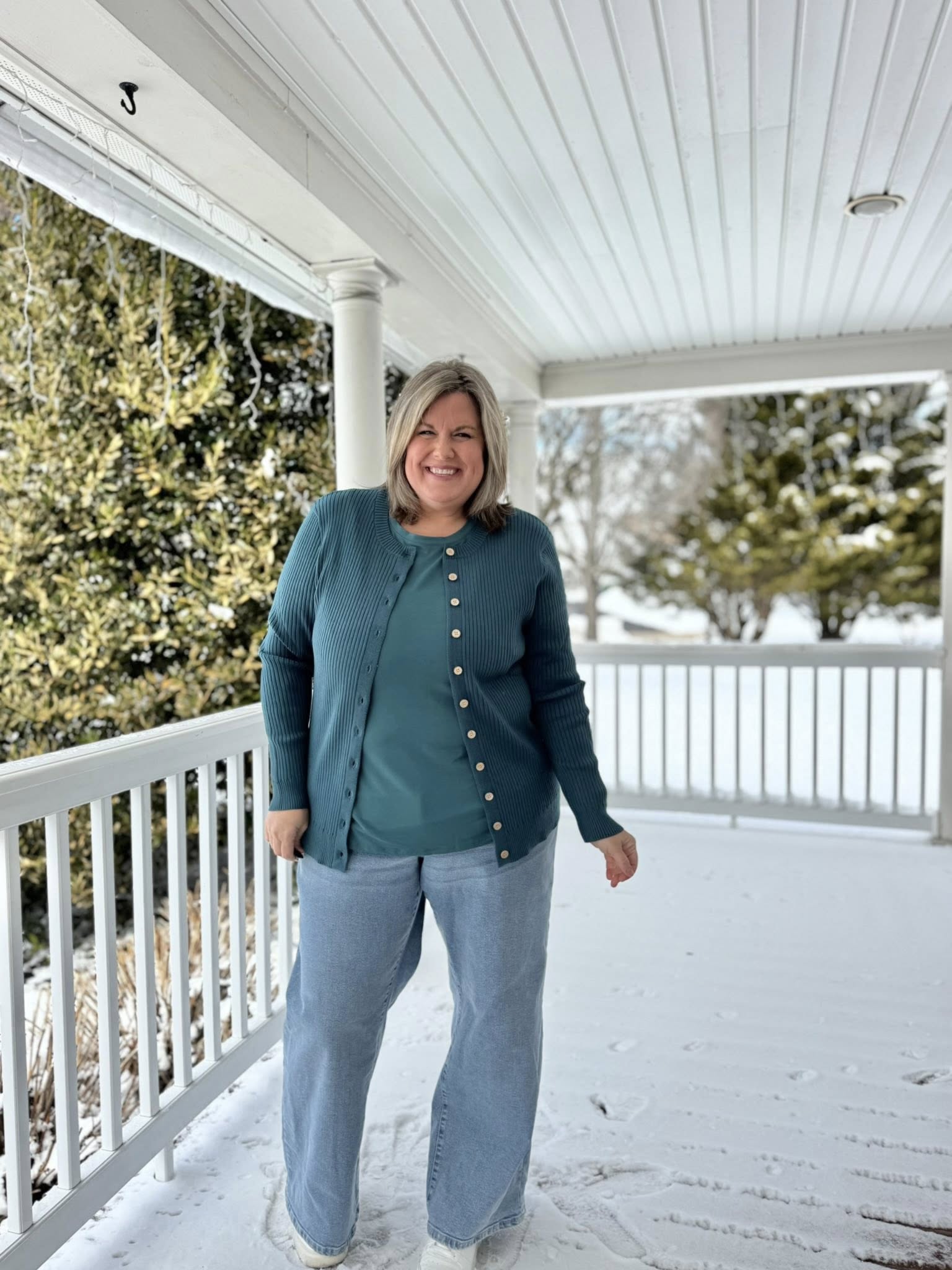 LuLaRoe Becky cardigan in solid evergreen teal rib knit with wooden buttons and fitted silhouette on a woman standing on a snow-covered porch wearing light blue jeans.