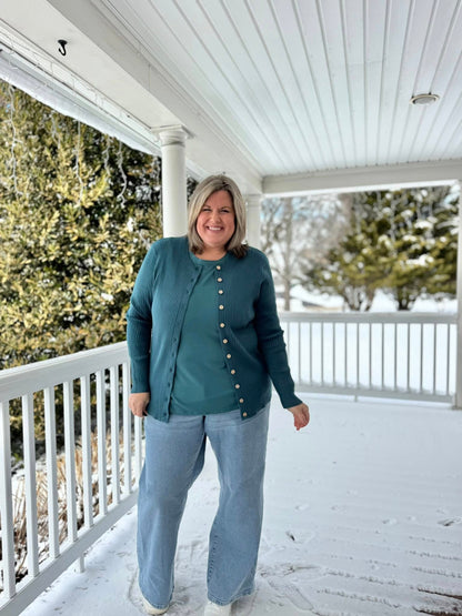 LuLaRoe Becky cardigan in solid evergreen teal rib knit with wooden buttons and fitted silhouette on a woman standing on a snow-covered porch wearing light blue jeans.