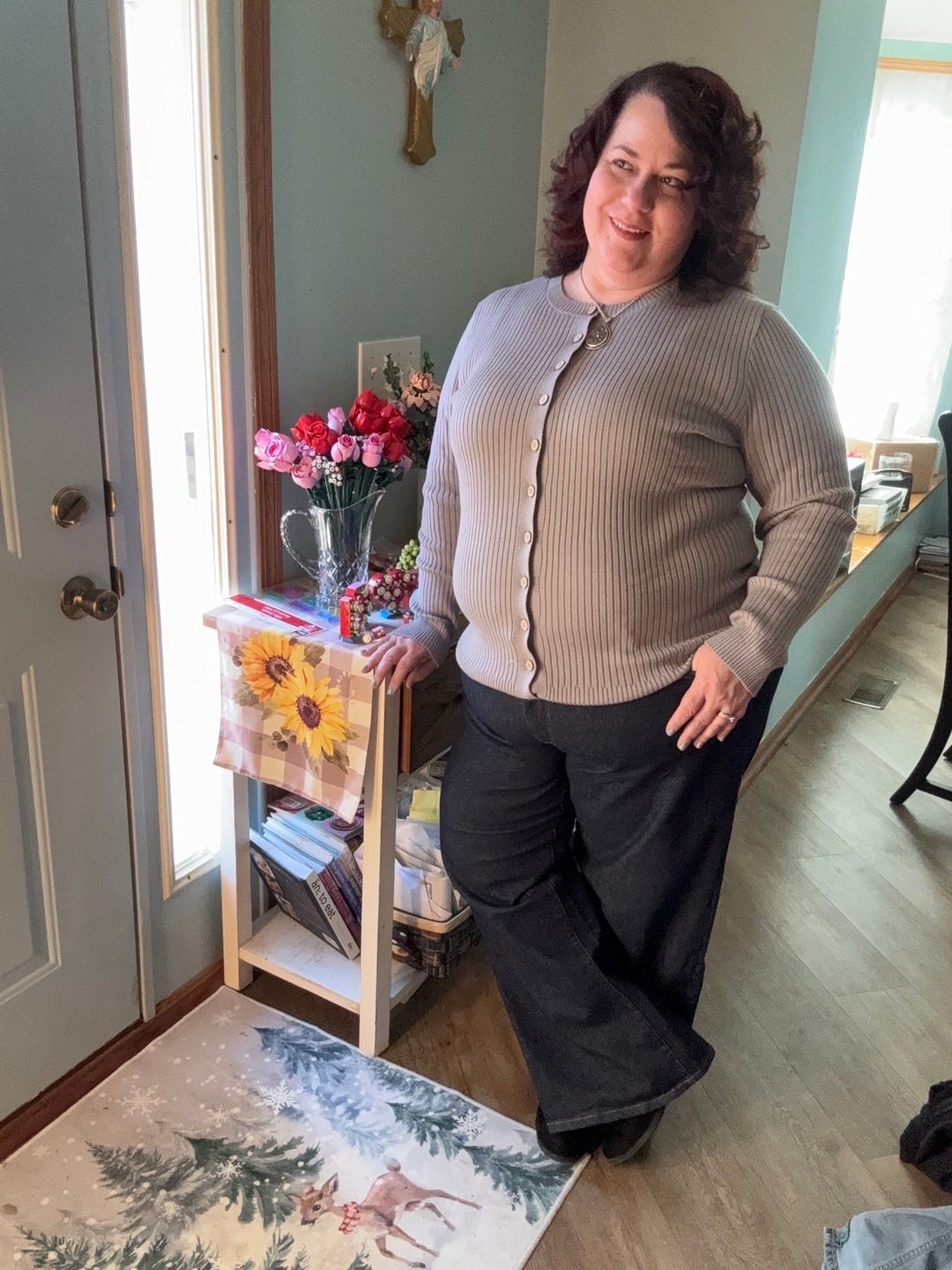 LuLaRoe Becky cardigan in solid soft dove gray rib knit with wooden buttons and fitted silhouette on a woman standing in a room with a bookshelf and decorative items.