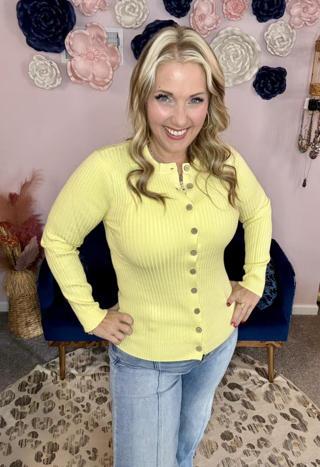 LuLaRoe Becky cardigan in solid soft lemon yellow rib knit with wooden buttons and fitted silhouette on a woman in a room with decorative flowers on the wall.