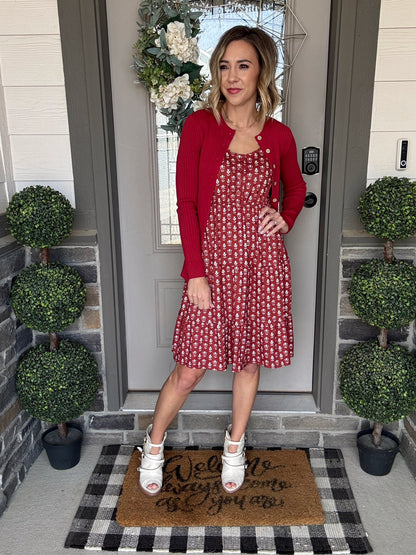 LuLaRoe Becky button cardigan in solid true red rib knit with wooden buttons and fitted silhouette on a woman in a red patterned dress standing on a doormat with decorative plants.