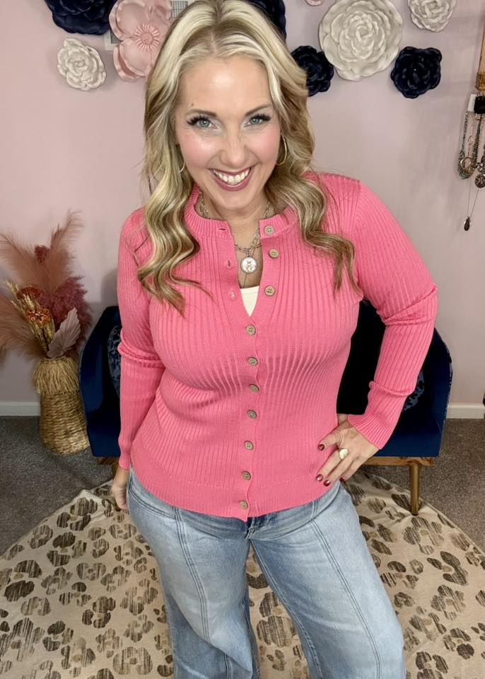 LuLaRoe Becky cardigan in solid watermelon pink rib knit with buttons and fitted silhouette  on a woman wearing blue jeans standing in front of decorative flowers on a wall.