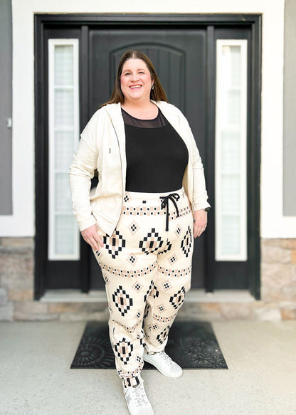 LuLaRoe Boyfriend Joggers in a cream and black geometric Aztec pattern worn by a model. Features a relaxed fit, drawstring waist, cuffed ankles, and soft knit fabric.