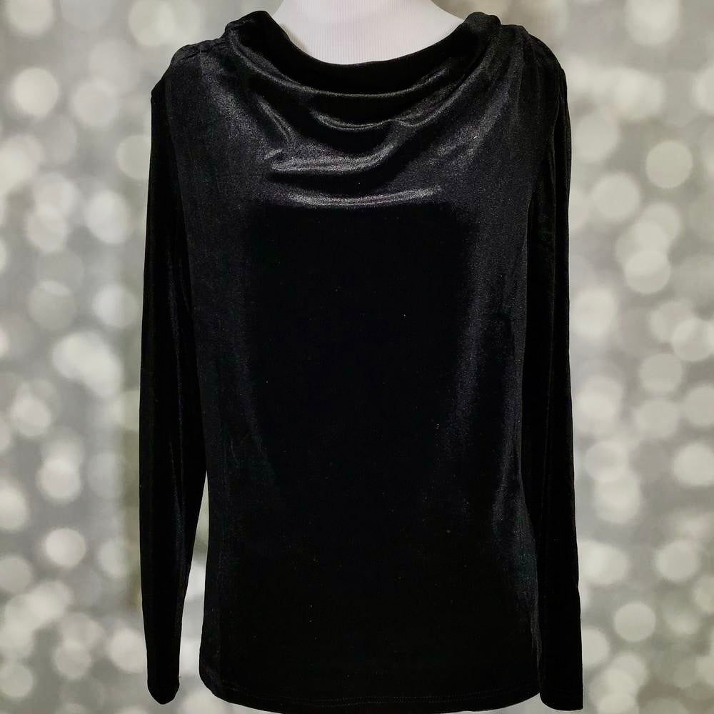 A black long-sleeve top with a draped, cowl-like neckline, displayed on a mannequin against a soft, out-of-focus bokeh background.