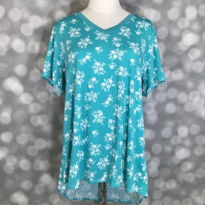 LuLaRoe Christy T in aqua blue featuring scattered white floral clusters with a relaxed V-neck silhouette displayed on a mannequin against a silver bokeh backdrop.