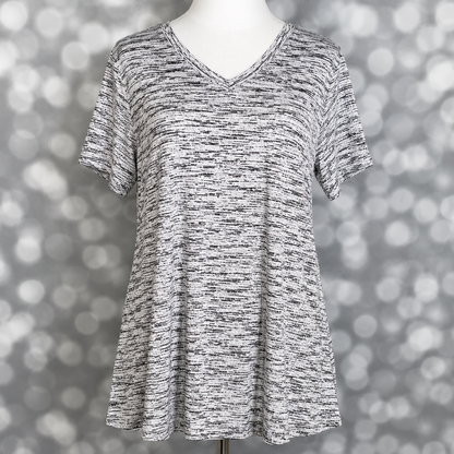 LuLaRoe Christy T relaxed swing top in black and white static heather print with subtle marled texture, v-neckline, short sleeves, and flowy silhouette displayed on mannequin against silver bokeh background.