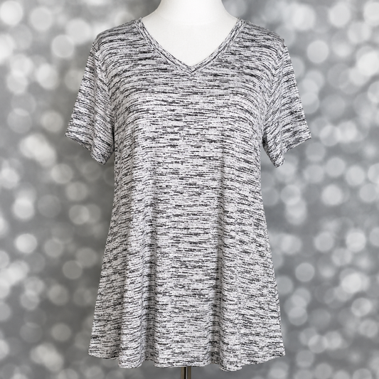 LuLaRoe Christy T relaxed swing top in black and white static heather print with subtle marled texture, v-neckline, short sleeves, and flowy silhouette displayed on mannequin against silver bokeh background.