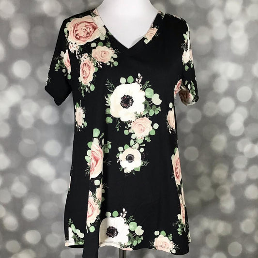 LuLaRoe Christy T featuring a black background with blush pink roses, ivory floral blooms, and soft green eucalyptus accents in a romantic floral print displayed on a mannequin against a silver bokeh background.