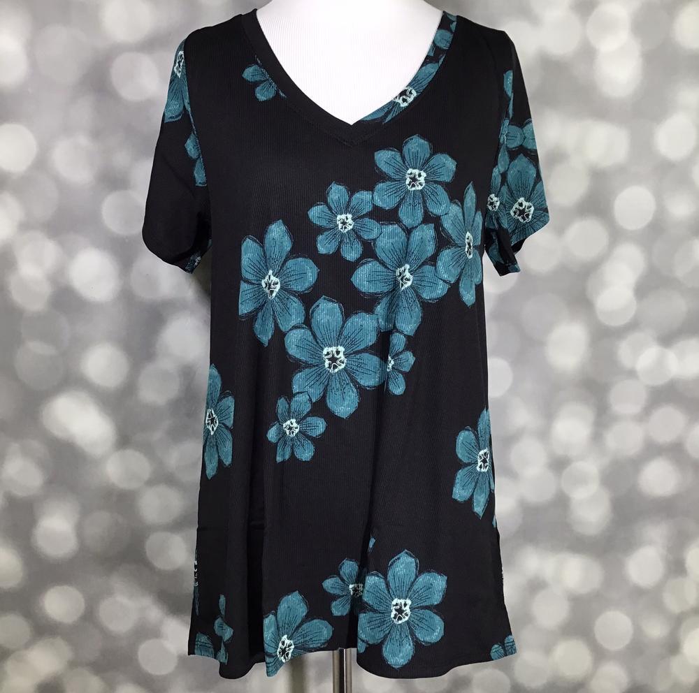 LuLaRoe Christy T featuring oversized teal blue floral blooms on a black background with a relaxed V-neck silhouette displayed on a mannequin against a silver bokeh backdrop.