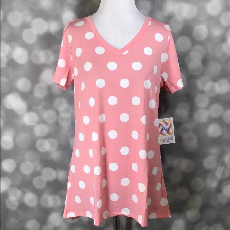 LuLaRoe Christy T featuring oversized white polka dots on a soft pink background with a relaxed V-neck silhouette displayed on a mannequin against a silver bokeh backdrop.