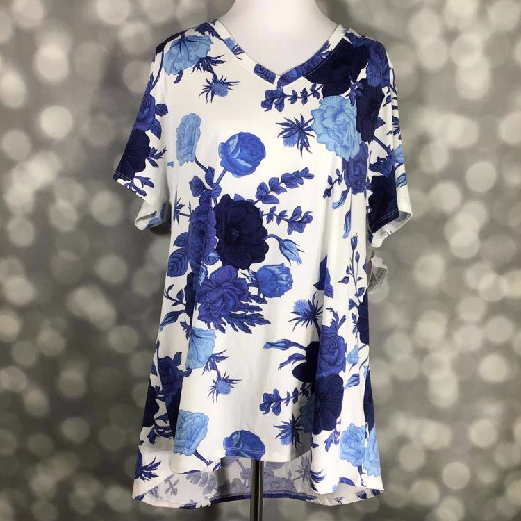 LuLaRoe Christy T featuring oversized sapphire blue and navy floral blooms on a white background with a relaxed V-neck swing silhouette displayed on a mannequin against a silver bokeh backdrop.