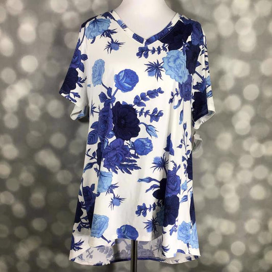 LuLaRoe Christy T featuring oversized sapphire blue and navy floral blooms on a white background with a relaxed V-neck swing silhouette displayed on a mannequin against a silver bokeh backdrop.