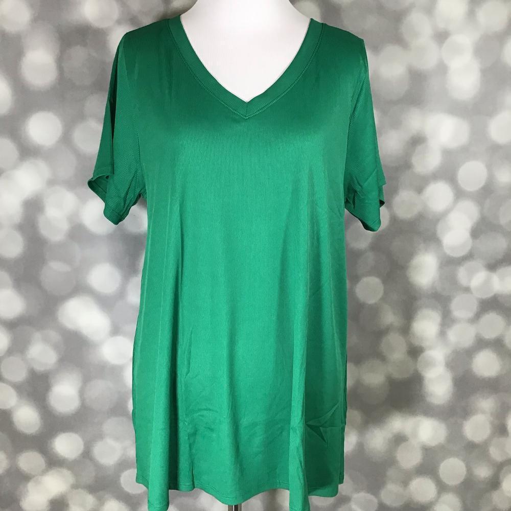 LuLaRoe Christy Tee in solid emerald green ribbed fabric displayed on a mannequin with a relaxed swing silhouette, short sleeves, and v-neckline against a soft gray bokeh background. Bright green boutique top with an easy everyday fit perfect for casual styling and layering.