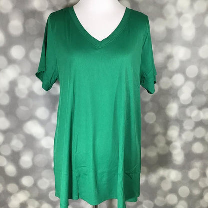 LuLaRoe Christy Tee in solid emerald green ribbed fabric displayed on a mannequin with a relaxed swing silhouette, short sleeves, and v-neckline against a soft gray bokeh background. Bright green boutique top with an easy everyday fit perfect for casual styling and layering.