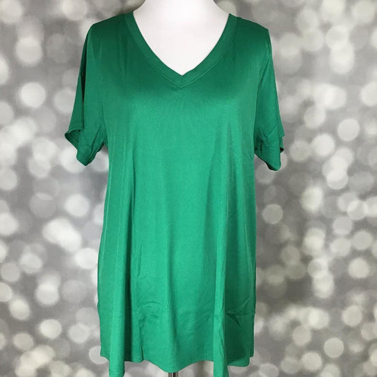 LuLaRoe Christy Tee in solid emerald green ribbed fabric displayed on a mannequin with a relaxed swing silhouette, short sleeves, and v-neckline against a soft gray bokeh background. Bright green boutique top with an easy everyday fit perfect for casual styling and layering.