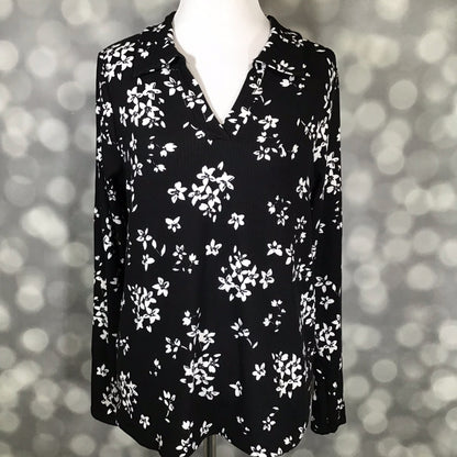 LuLaRoe Courtney Long Sleeve Polo Top in black with white scattered floral print, displayed on a mannequin against a soft light-bokeh background. Features a classic polo collar, V-notch neckline, long sleeves, and a comfortable draped fit in soft 4x2 Rib Brushed fabric.