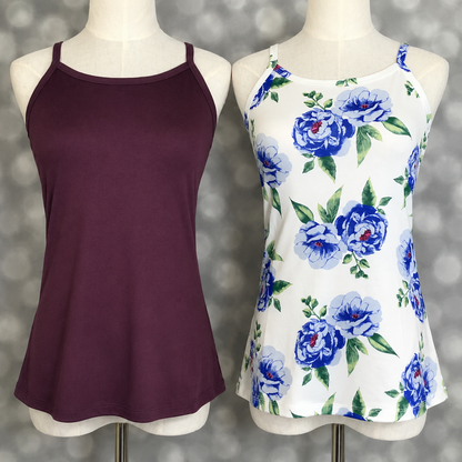 Two LuLaRoe Essential camis photographed on mannequins featuring a solid deep plum camisole and a white cami with oversized blue watercolor rose floral print and green leaves against a neutral gray studio backdrop.