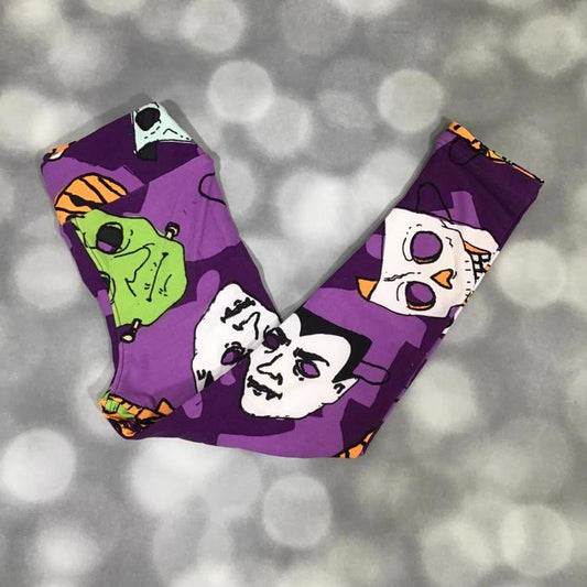 LuLaRoe Halloween leggings in purple featuring classic monster faces in green, white, and orange with spooky details.

